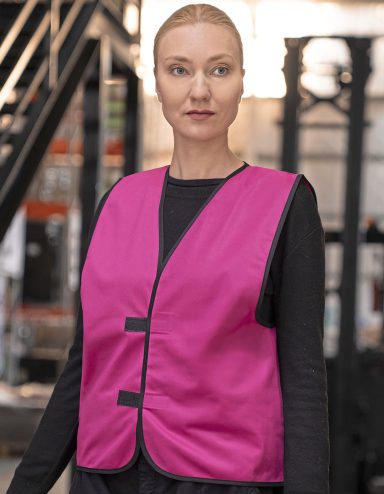 Frau trägt eine pinke Weste über einem schwarzen Oberteil in einem industriellen Umfeld.
