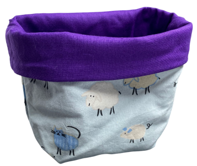 Körbchen mit lila Rand und Schafmotiven auf hellblauem Stoff.