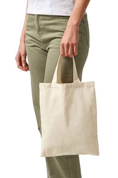 Beige Tragetasche aus Stoff, gehalten von einer Person mit grünen Hosen.