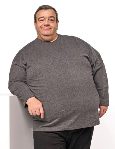 Mann in grauem Sweatshirt, lächelnd, mit einer Hand auf einem weißen Podest.