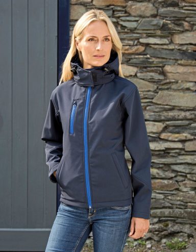 Frau in blauer Jacke mit Kapuze vor einer Steinmauer.