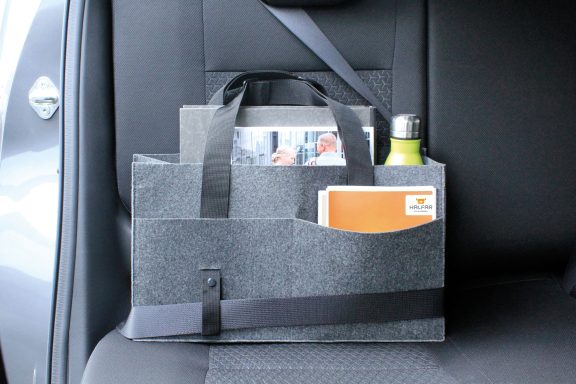 Schwarze Tasche mit Fächern für Zeitschriften und Getränke an einem Fahrzeugsitz.