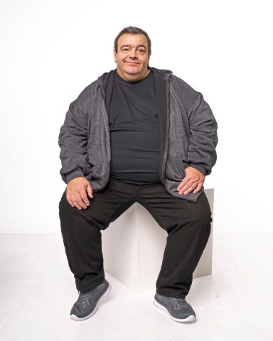 Mann mit kurzer dunkler Hose und grauer Jacke sitzt auf einem weißen Block.