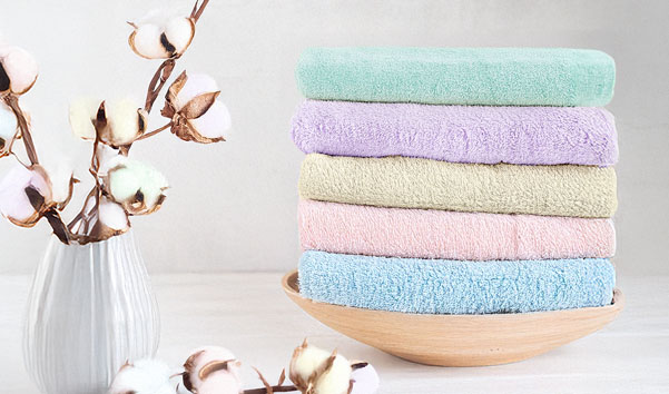 Gestapelte Handtücher in sanften Farben in einer Holtschale, neben einer Vase mit Baumwollzweigen.