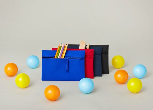 Bunte Bälle um drei Taschen in Blau, Rot und Schwarz mit Stiften.
