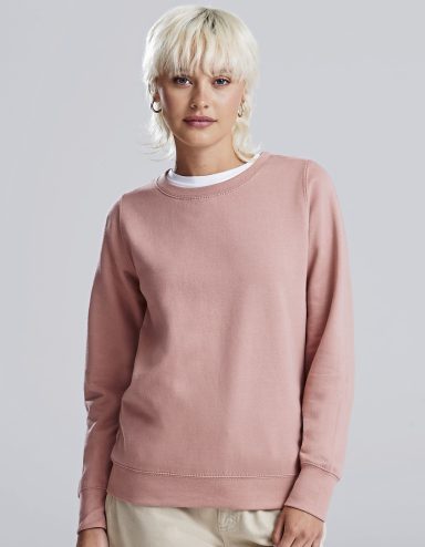 Frau mit blonden, kurzen Haaren trägt einen rosa Pullover und schaut direkt in die Kamera.