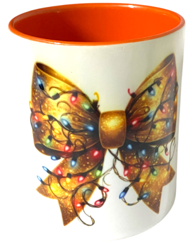 Tasse mit goldener Schleife und bunten Lichtern auf creamfarbenem Hintergrund.