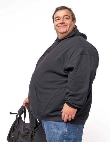 Männlicher Erwachsener mit grauem Sweatshirt und Tasche, lächelt freundlich.