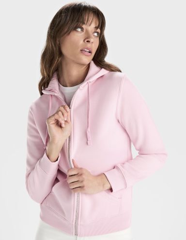 Eine Frau trägt einen rosa Hoodie mit Reißverschluss und schaut nachdenklich zur Seite.