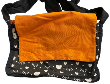 Schwarze Umhängetasche mit orangefarbener Klappe und herzförmigem Muster.